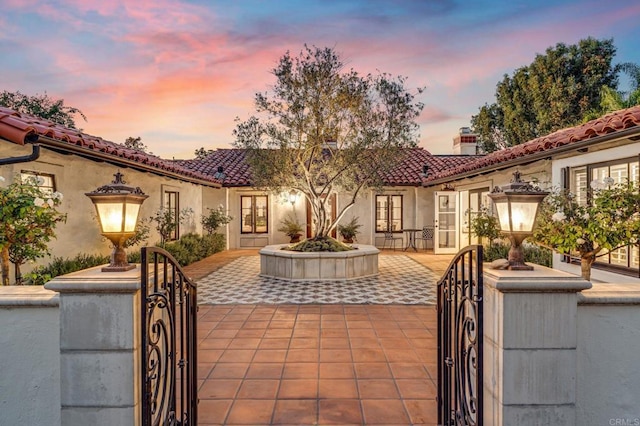 mediterranean / spanish-style house featuring french doors, stucco siding, a gate, a patio area, and a tiled roof