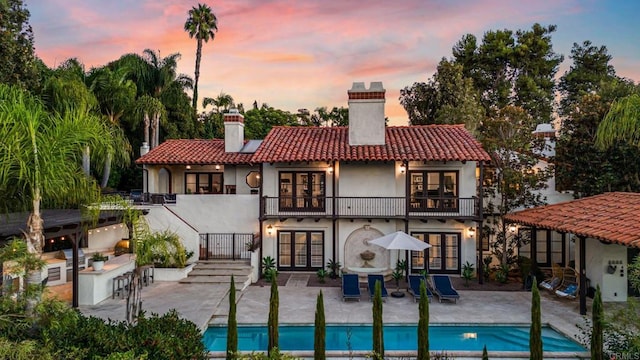 rear view of house featuring a patio, a balcony, a tile roof, outdoor dry bar, and french doors