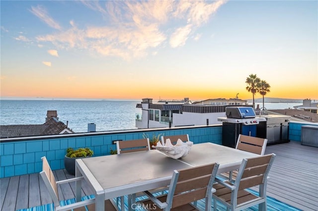 deck with outdoor dining space, a water view, and a grill