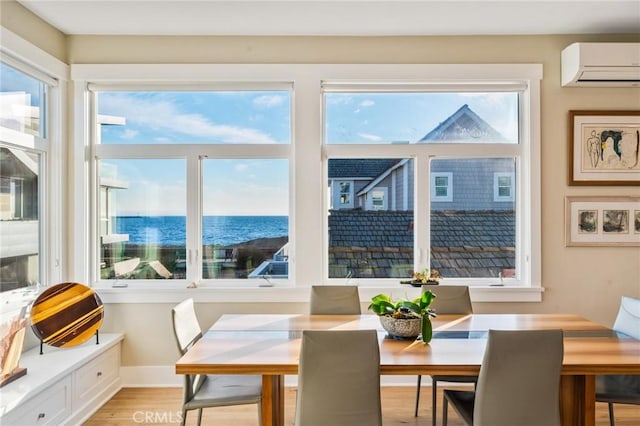 dining room featuring baseboards, a wall unit AC, a water view, and light wood-style floors