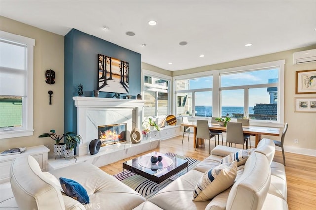 living area featuring baseboards, a high end fireplace, a wall unit AC, light wood-style flooring, and recessed lighting