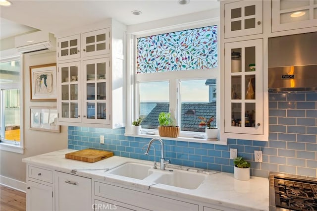 kitchen with light stone counters, white cabinetry, sink, and a wall unit AC