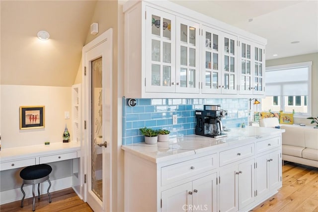 kitchen featuring glass insert cabinets, light wood-style floors, white cabinetry, and decorative backsplash