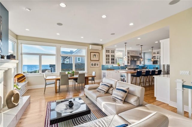 living room with a water view, a healthy amount of sunlight, an AC wall unit, and light hardwood / wood-style floors