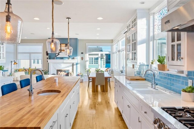 kitchen featuring ventilation hood, white cabinetry, sink, wooden counters, and hanging light fixtures