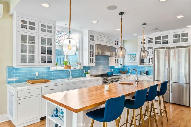 kitchen with stainless steel appliances, white cabinetry, a kitchen island with sink, and range hood