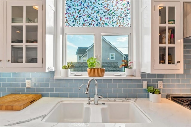 kitchen with light stone counters, sink, tasteful backsplash, and white cabinets