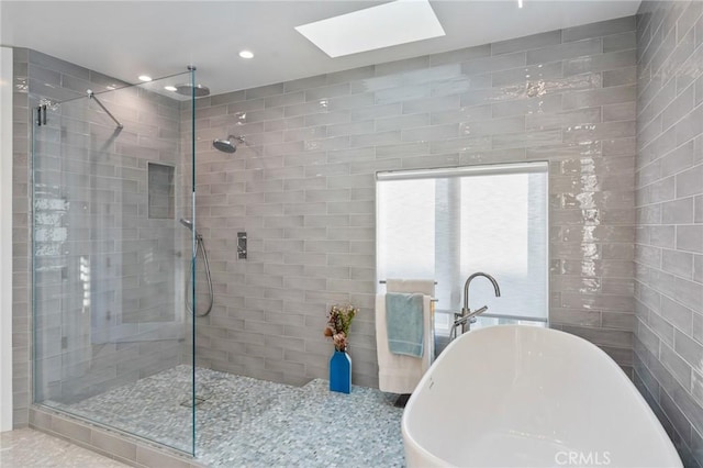 bathroom featuring a skylight, a shower stall, a freestanding bath, and recessed lighting