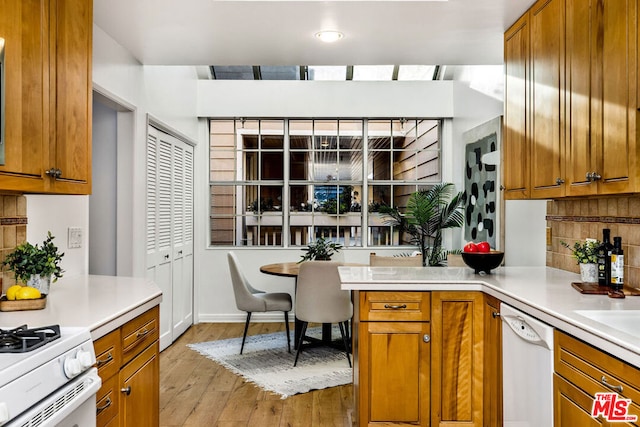 kitchen featuring kitchen peninsula, white appliances, decorative backsplash, and light hardwood / wood-style flooring