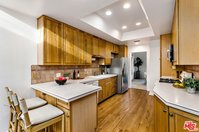 kitchen featuring kitchen peninsula, appliances with stainless steel finishes, light wood-type flooring, a tray ceiling, and a breakfast bar