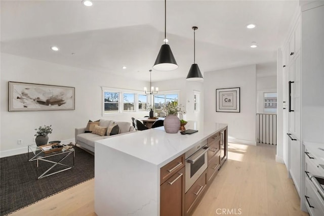 kitchen with pendant lighting, white cabinets, light wood-type flooring, and a kitchen island