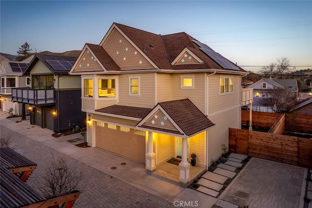 view of front of property featuring decorative driveway, roof with shingles, solar panels, fence, and a garage