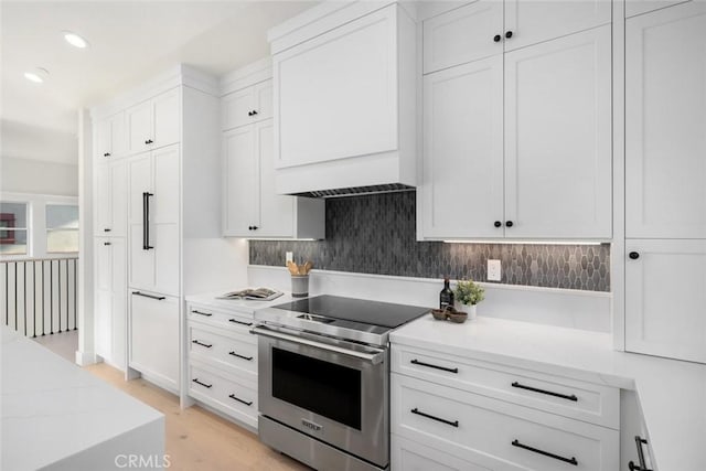 kitchen with white cabinetry, light hardwood / wood-style floors, electric stove, light stone counters, and custom range hood