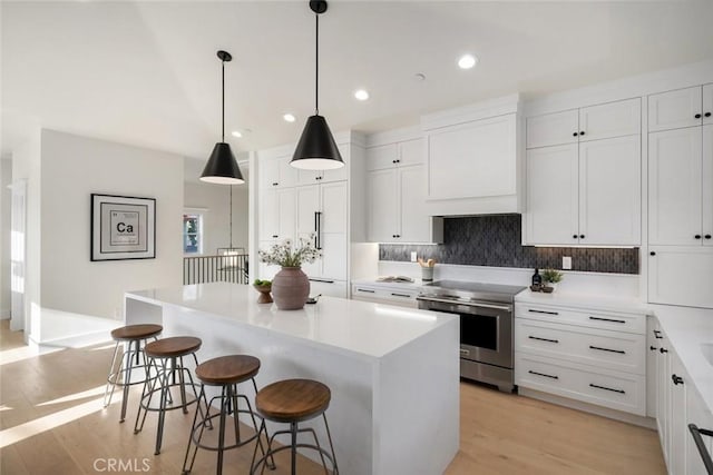 kitchen with a breakfast bar, custom range hood, light wood-style floors, white cabinetry, and stainless steel electric range