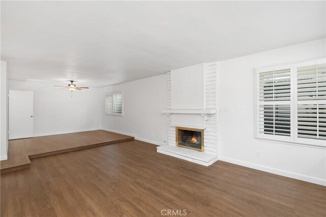 unfurnished living room featuring a brick fireplace, dark hardwood / wood-style flooring, a healthy amount of sunlight, and ceiling fan