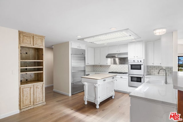 kitchen with white cabinets, a kitchen island, stainless steel appliances, sink, and light hardwood / wood-style flooring