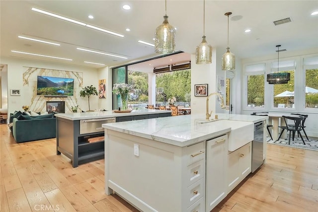 kitchen featuring light stone countertops, white cabinets, decorative light fixtures, sink, and a kitchen island with sink