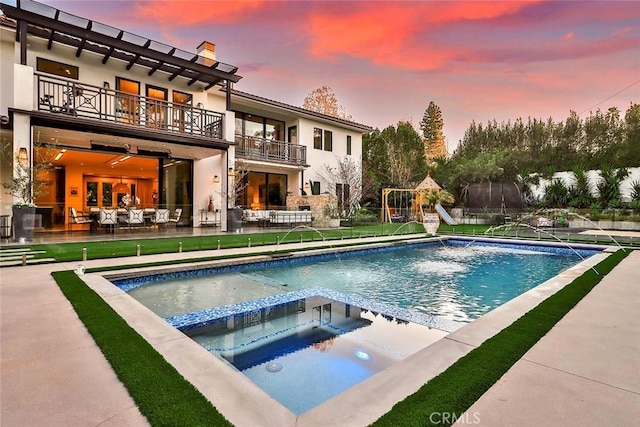 pool at dusk featuring pool water feature and an in ground hot tub