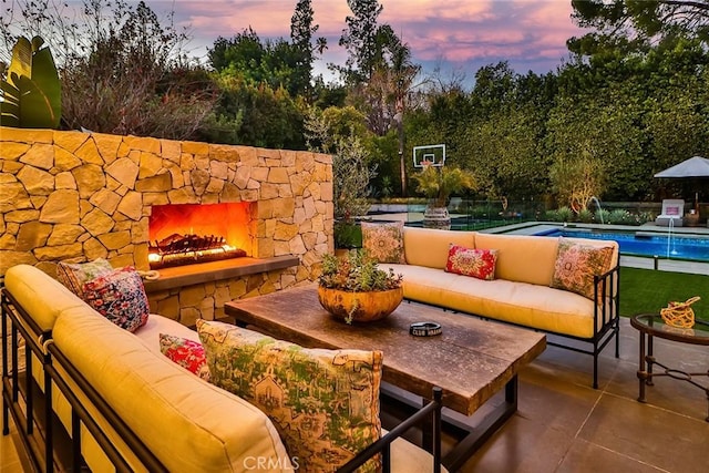 patio terrace at dusk with pool water feature and an outdoor living space with a fireplace