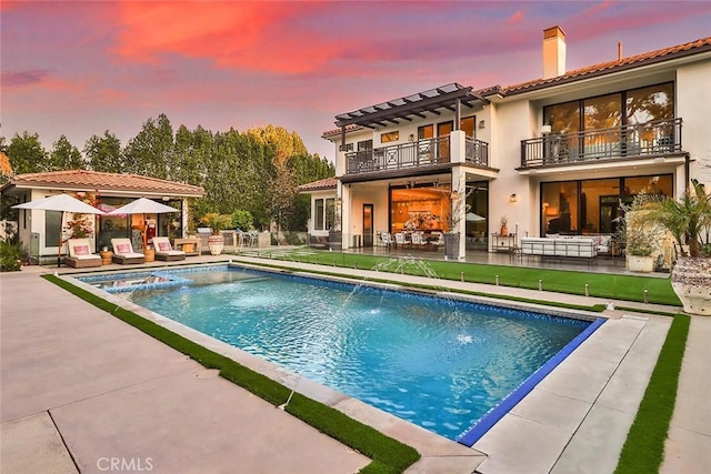 pool at dusk featuring pool water feature and a patio