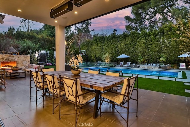 patio terrace at dusk with a fenced in pool, pool water feature, and an outdoor stone fireplace