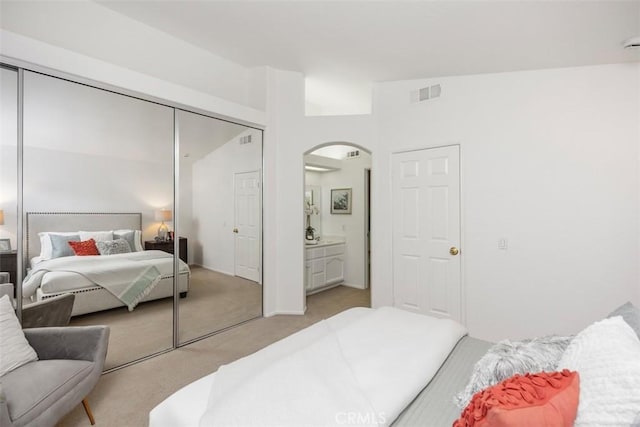 bedroom with lofted ceiling, light carpet, a closet, and ensuite bathroom