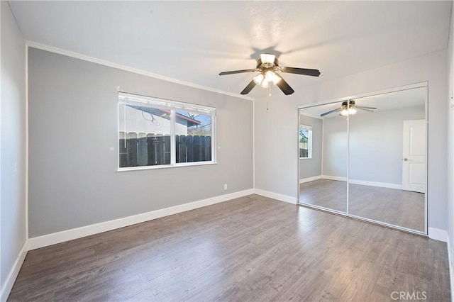 unfurnished bedroom with ceiling fan, a closet, hardwood / wood-style floors, and multiple windows