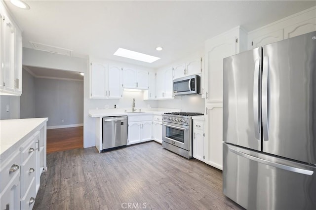 kitchen featuring a skylight, white cabinetry, light hardwood / wood-style floors, appliances with stainless steel finishes, and sink