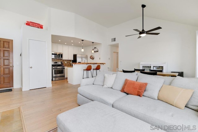 living room with high vaulted ceiling, ceiling fan, and light wood-type flooring