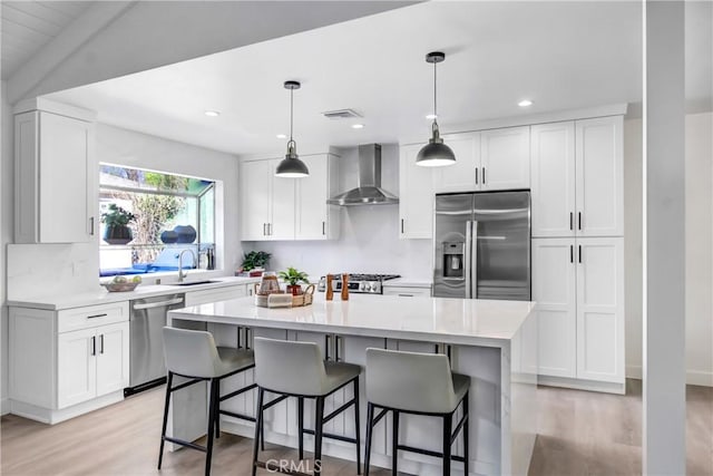 kitchen featuring appliances with stainless steel finishes, pendant lighting, wall chimney exhaust hood, white cabinets, and a center island