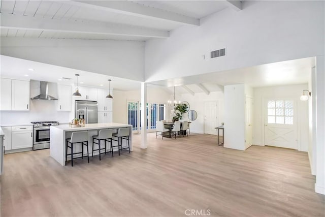 kitchen with a breakfast bar, a kitchen island with sink, appliances with stainless steel finishes, white cabinets, and wall chimney exhaust hood