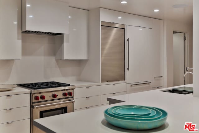 kitchen featuring high end stainless steel range oven, premium range hood, and white cabinetry