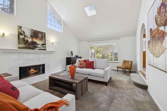 carpeted living room featuring a fireplace, a skylight, and high vaulted ceiling