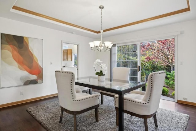 dining room with a raised ceiling, crown molding, dark wood-type flooring, and an inviting chandelier