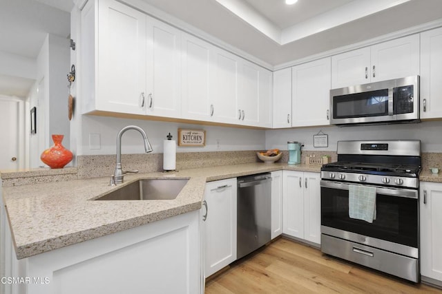 kitchen with white cabinetry, stainless steel appliances, light wood-type flooring, light stone countertops, and sink