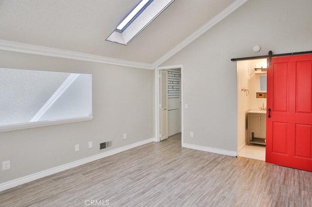 interior space with vaulted ceiling with skylight, light hardwood / wood-style flooring, sink, and a barn door