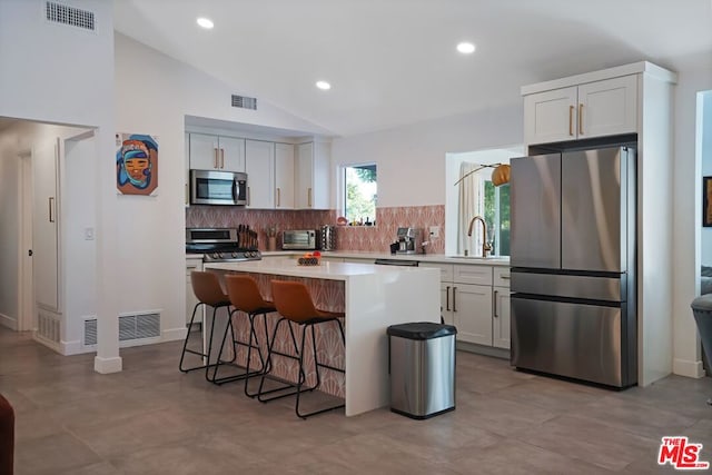 kitchen with lofted ceiling, white cabinets, stainless steel appliances, and a kitchen island