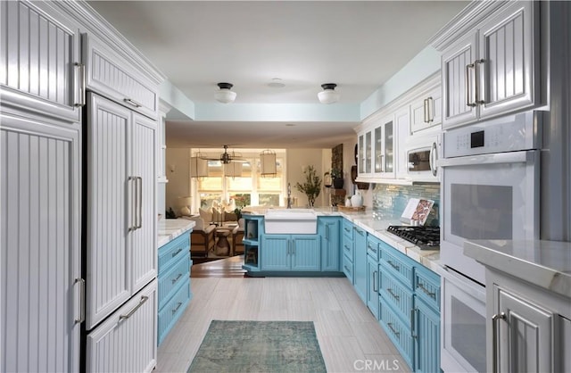 kitchen with kitchen peninsula, decorative backsplash, sink, white cabinets, and blue cabinets