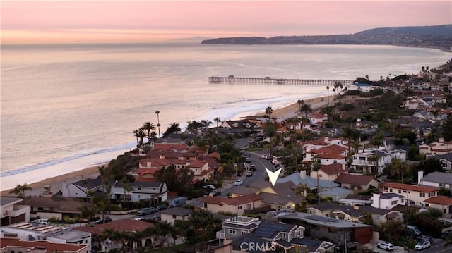 aerial view at dusk featuring a water view and a view of the beach