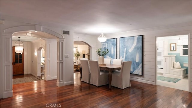 dining space with dark wood-type flooring, crown molding, and ornate columns