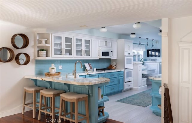 kitchen featuring white cabinetry, backsplash, white appliances, a kitchen breakfast bar, and blue cabinets