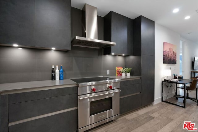 kitchen with light wood-type flooring, wall chimney exhaust hood, and designer range