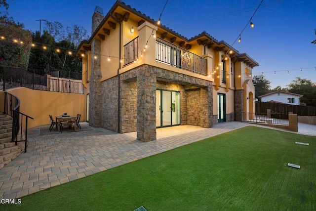 back house at dusk featuring a patio, a balcony, and a yard