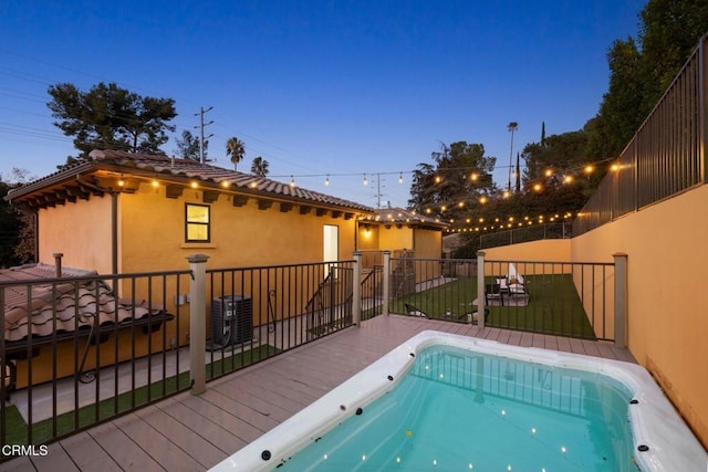 pool at dusk featuring central AC, a deck, and a lawn