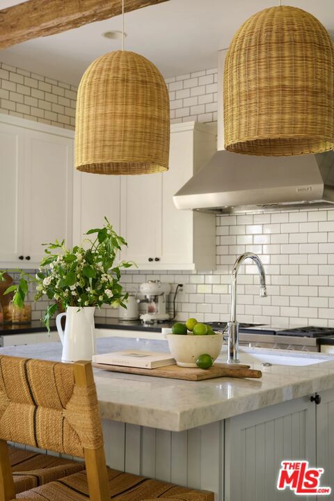 kitchen featuring tasteful backsplash, wall chimney range hood, a breakfast bar, light stone countertops, and white cabinets