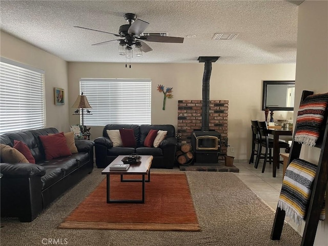 living room featuring ceiling fan, light tile patterned flooring, a wood stove, and a textured ceiling