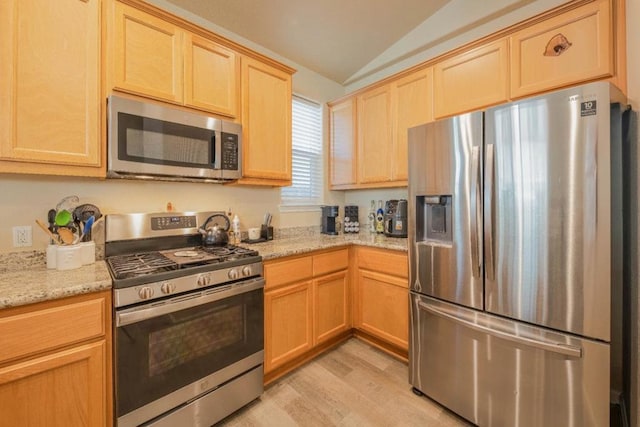 kitchen with appliances with stainless steel finishes, light stone countertops, vaulted ceiling, and light wood-type flooring