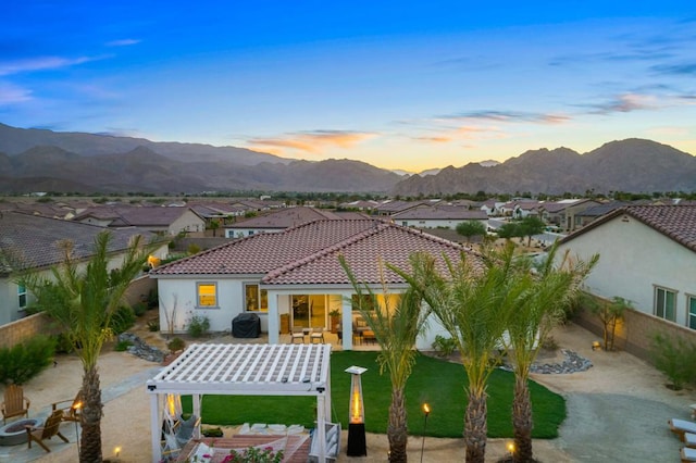 back house at dusk featuring a mountain view, a pergola, a patio area, and a yard