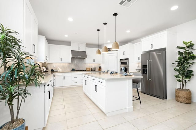 kitchen featuring appliances with stainless steel finishes, hanging light fixtures, backsplash, white cabinets, and a kitchen island