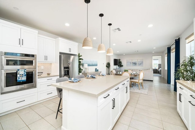 kitchen featuring appliances with stainless steel finishes, white cabinetry, a kitchen island, a kitchen bar, and decorative light fixtures